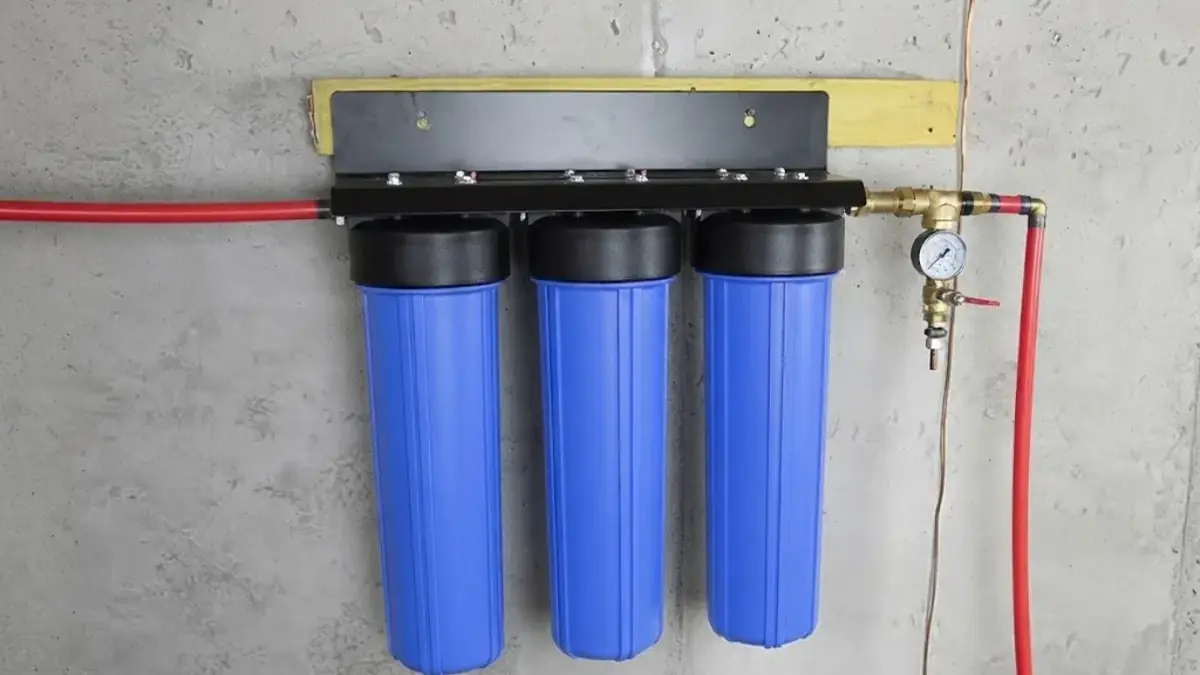 Three blue whole house water filter housings mounted on a concrete wall with red tubing