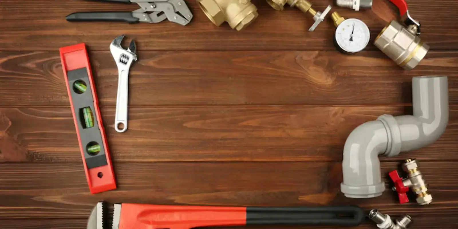 Plumbing tools and fittings on a wooden surface including a level, wrenches, valves and pipe elbow